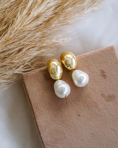 two pairs of gold and white pearl earrings on top of a brown box next to some dry grass