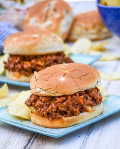 two sloppy joe sandwiches on blue plates with chips