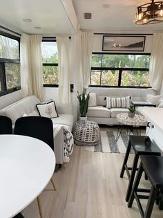 a living room filled with white furniture and lots of windows next to a dining table