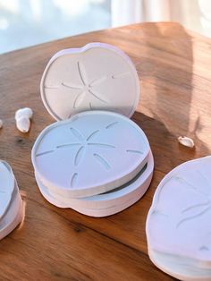 four white plates sitting on top of a wooden table next to shells and seashells