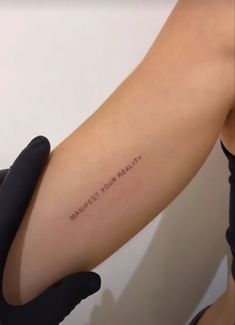 a woman's arm with the words manies your reality tattooed on her left arm