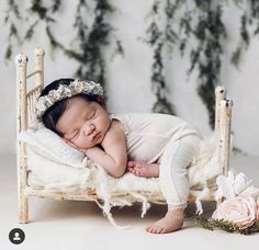 a baby is sleeping on a bed with white fur and flowers in her hair, wearing a flower headband