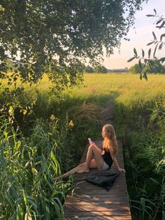 a woman sitting on a wooden bridge in the middle of a field looking at her cell phone