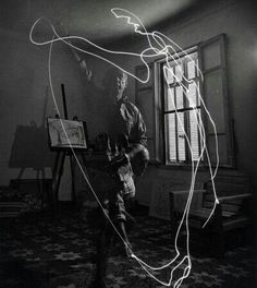 a black and white photo of a man standing in front of a window with light painting on the floor