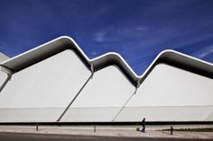 a man walking down the street in front of a white building with triangular shaped windows