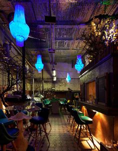 an empty restaurant with blue and green lights hanging from the ceiling, along with many chairs