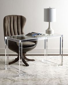 a glass desk with a chair and lamp on it in front of a white wall