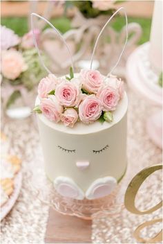 a white cake with pink roses and bunny ears on it's top sitting on a table