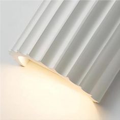 a white light that is on the side of a wall with pleated curtains behind it