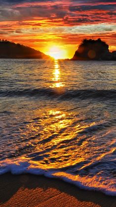 the sun is setting over the ocean with waves coming in to shore and an island in the distance