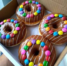 four donuts with chocolate frosting and sprinkles in a cardboard box