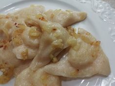 three dumplings on a white plate covered in cheese and onions, ready to be eaten