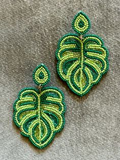 two green and yellow beaded earrings sitting on top of a gray cloth covered surface