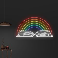 an open book sitting on top of a table next to a neon sign that reads rainbow