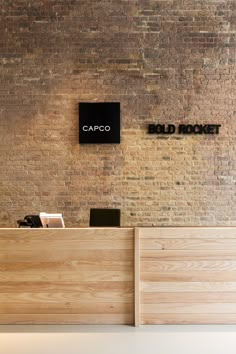 the front desk of an office with a brick wall and black sign on it's side