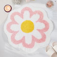 a pink and white rug with a flower on it next to candles, sandals and other items