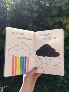 someone is holding up an open book with pictures of clouds, stars and rainbows