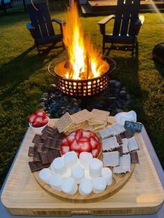 a fire pit with marshmallows, strawberries and chocolate on the table