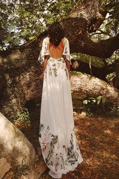 a woman standing in front of a tree wearing a white dress with flowers on it