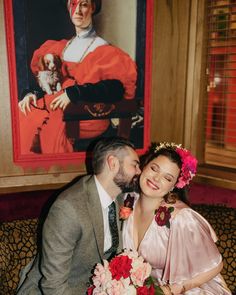 a man and woman sitting next to each other in front of a painting on the wall