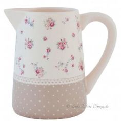 a white pitcher with pink flowers and polka dots on the bottom, sitting in front of a white background