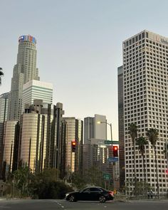 a car is driving down the street in front of tall buildings and palm trees on either side