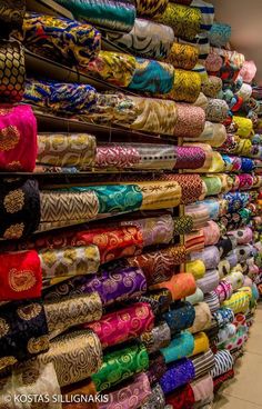 many different types of scarves are stacked on the wall in front of each other