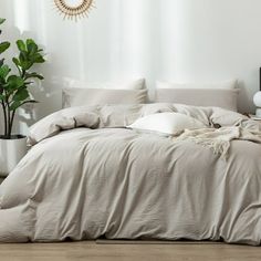 an unmade bed with white sheets and pillows in a room next to a potted plant