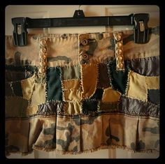 a camouflage skirt hanging on a wall with buttons and chains attached to the bottom of it