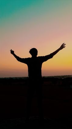 the silhouette of a person with their arms outstretched in front of an orange and blue sky