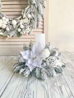 a white christmas wreath on top of a wooden table next to a candle and some decorations