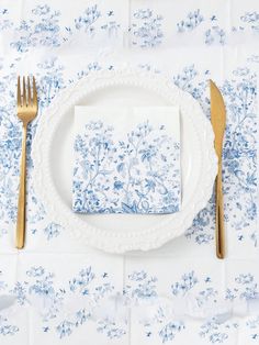 a place setting with blue and white floral napkins, silverware and gold forks