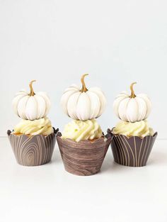 three cupcakes with white frosting and pumpkin decorations