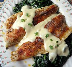 two pieces of chicken covered in white sauce and spinach on a plate with a floral border