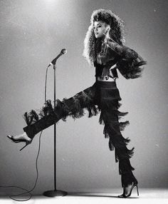 a woman standing in front of a microphone with her legs spread out and wearing feathered pants