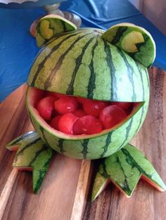 a watermelon shaped like a frog with its mouth open and some cherries in it