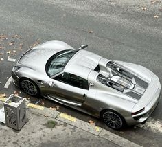 a silver sports car parked on the side of the road next to a trash can