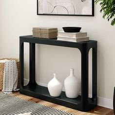 a black table with two white vases on it in front of a framed painting