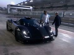 two men standing next to a black sports car