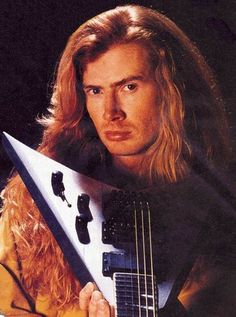 a man holding a guitar in his right hand and looking at the camera with an intense look on his face