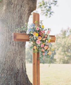 a cross with flowers on it next to a tree