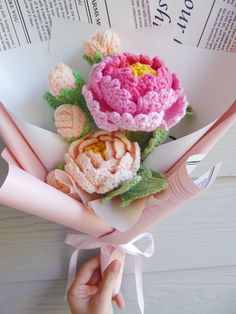 crocheted flowers are being held by someone's hand on top of an open book