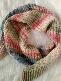 a multicolored knitted scarf laying on top of a white bed coverlet