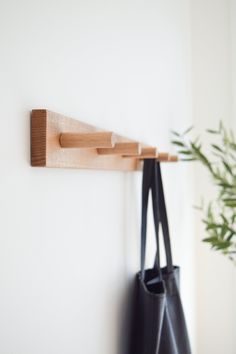 a black bag hanging on a white wall next to a wooden coat rack and plant