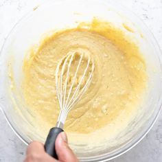 someone mixing batter in a glass bowl with a whisk on the side,