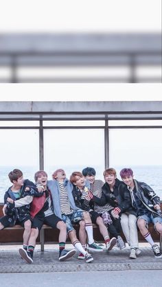 a group of young men sitting on top of a wooden bench next to the ocean