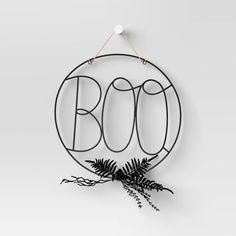 a round metal sign with the word boo on it and a fern in front of it