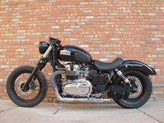 a black motorcycle parked next to a brick wall