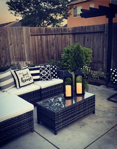 an outdoor living area with couches, tables and pillows on the ground in front of a wooden fence