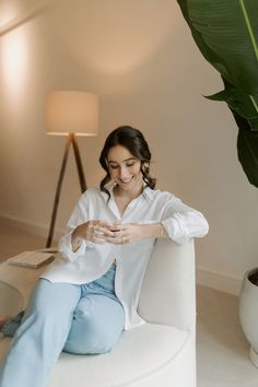 a woman sitting on a white couch looking at her cell phone while wearing blue jeans